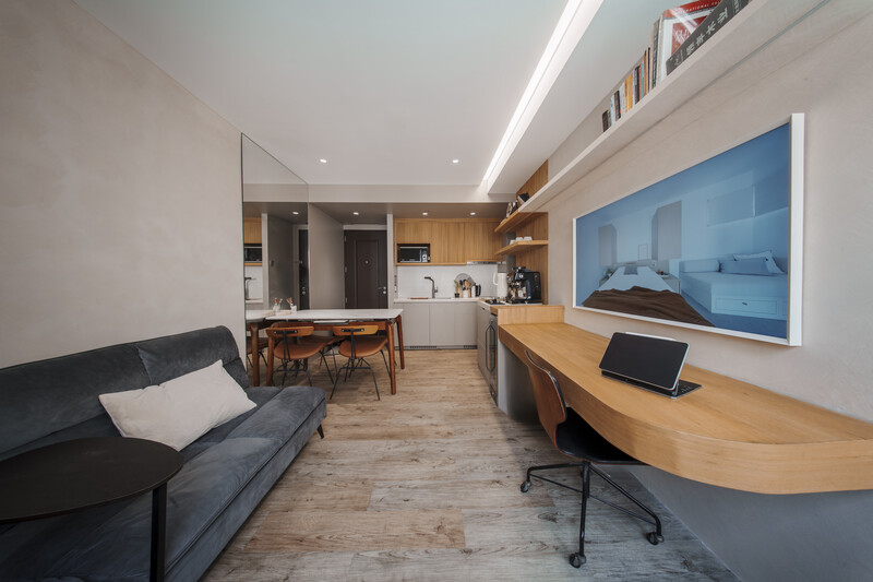 Modern open-plan apartment interior with kitchen, living area, and workspace along a wood-floored corridor.