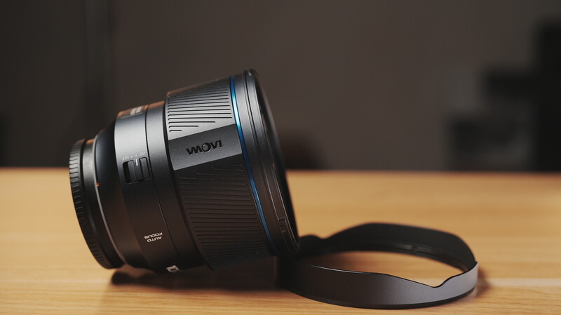 Telephoto lens with blue accent ring and lens cap on wooden surface.