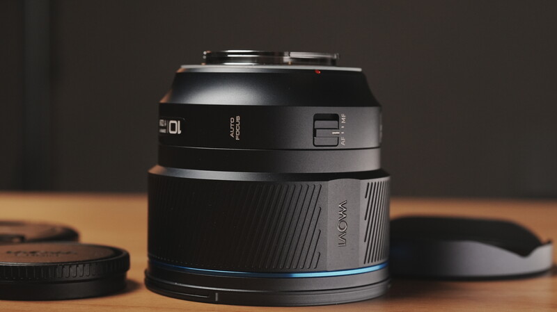 Camera lens with black barrel and blue accent ring displayed on wooden surface with lens caps nearby.