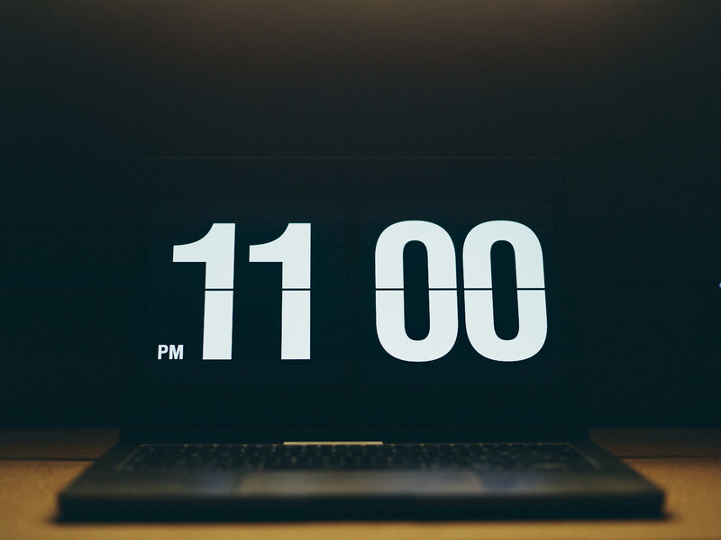 Digital clock display showing 11:00 PM on a dark background above a laptop keyboard.
