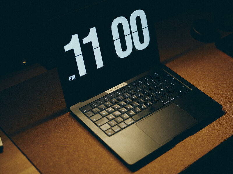 Laptop displaying 11:00 PM on its screen, positioned open on a wooden surface in warm lighting.