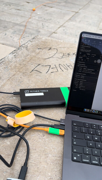Laptop, external hard drive, and color checker card arranged on architectural blueprints.