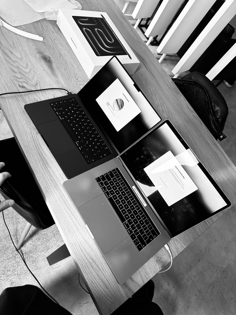 Overhead view of two laptops and mobile devices on a wooden desk in black and white.
