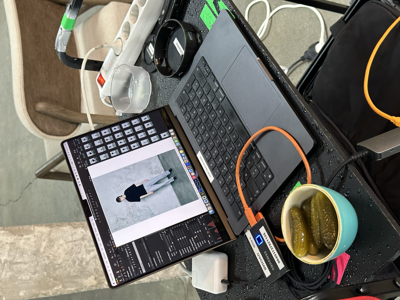 Overhead view of a creative workspace with laptops, headphones, keyboard, and a cup of tea on a dark mat.