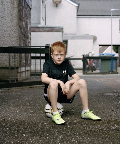 Young child with reddish hair crouching on pavement in an indoor sports facility.