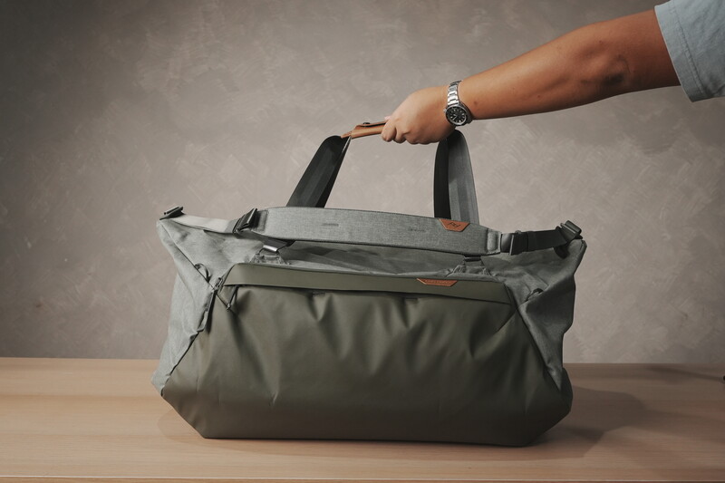 Person holding olive-green camera bag with dual handles against neutral background.