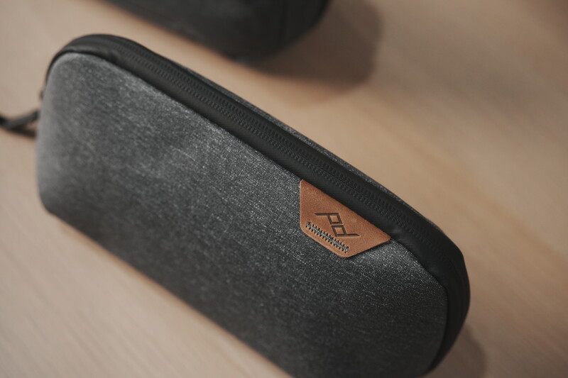 Gray fabric carrying case with black zipper and tan leather brand patch on wooden surface.