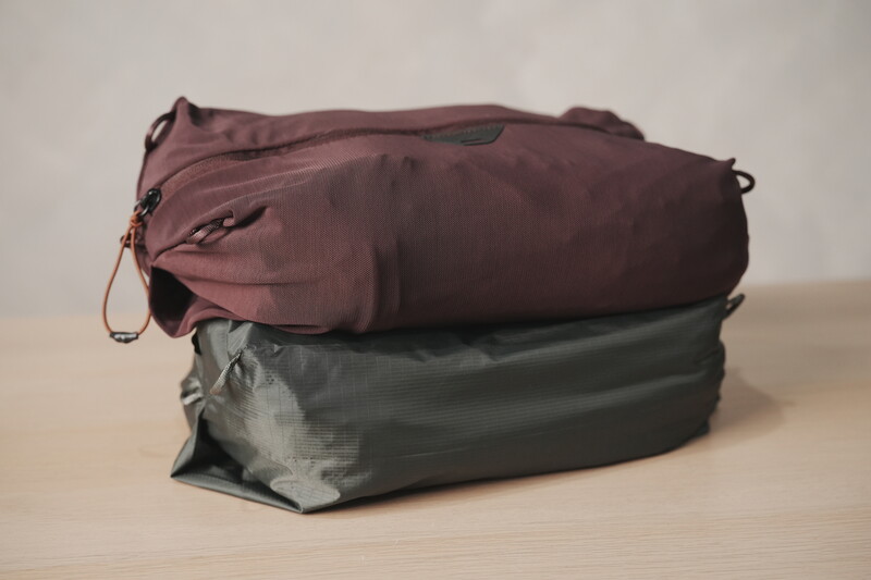 Two packed stuff sacks in burgundy and olive green stacked on a wooden surface.