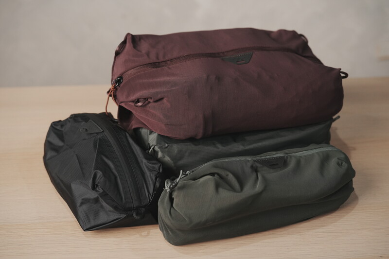 Three packed travel bags stacked on a wooden surface: burgundy, black, and olive green.
