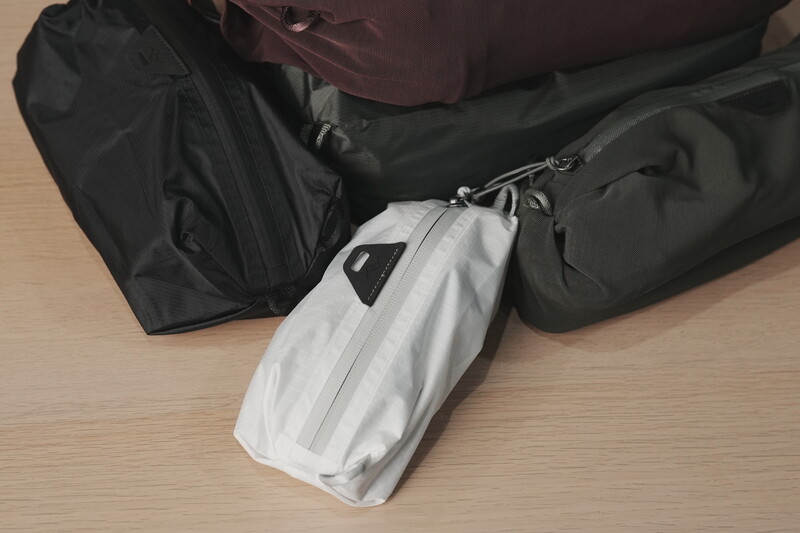 Travel packing arrangement showing a white cable organizer pouch surrounded by black and dark-colored compression bags on a wooden surface.