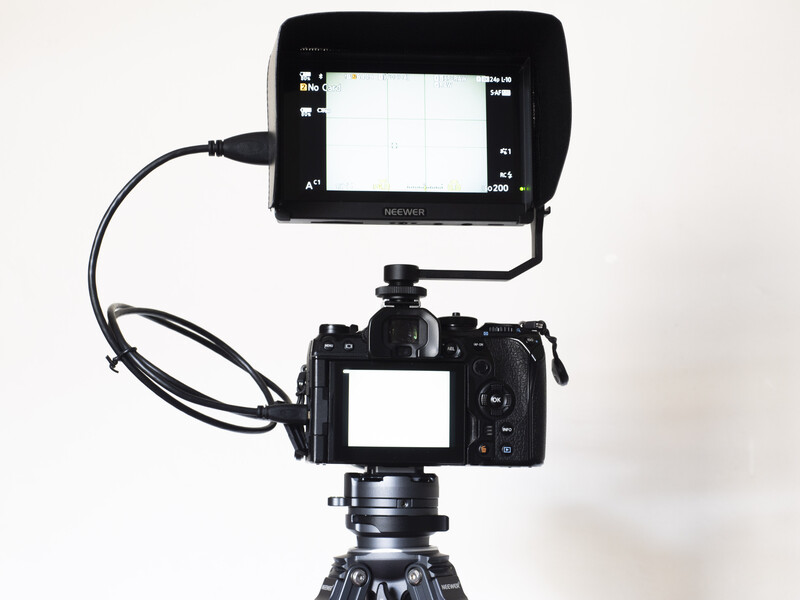 Professional video camera mounted on tripod with external monitor connected via cable.