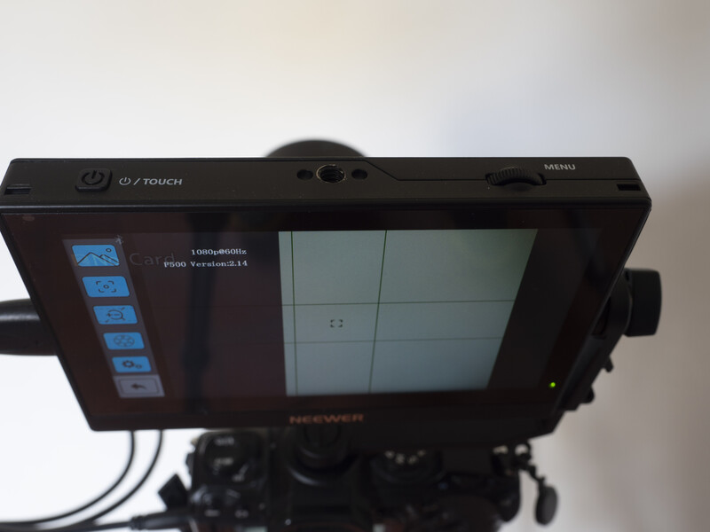 Monitor with grid display and blue control buttons mounted on camera rig.