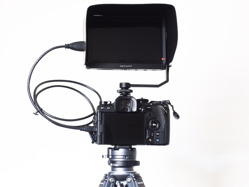 Professional camera mounted on tripod with external monitor and cable connection.