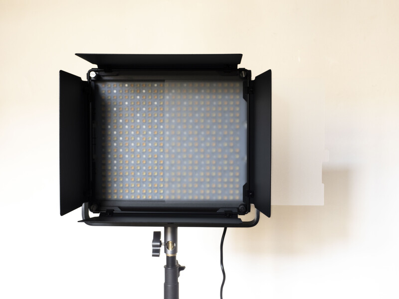 Professional LED panel light with barndoors mounted on a stand, showing blue-tinted light panel and power cable.
