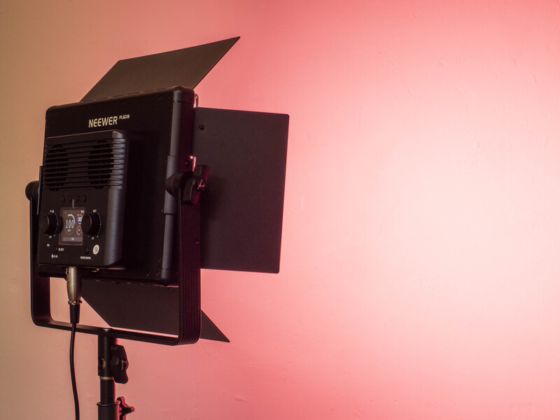 Professional LED panel light with barn doors mounted on a stand against a pink gradient background.