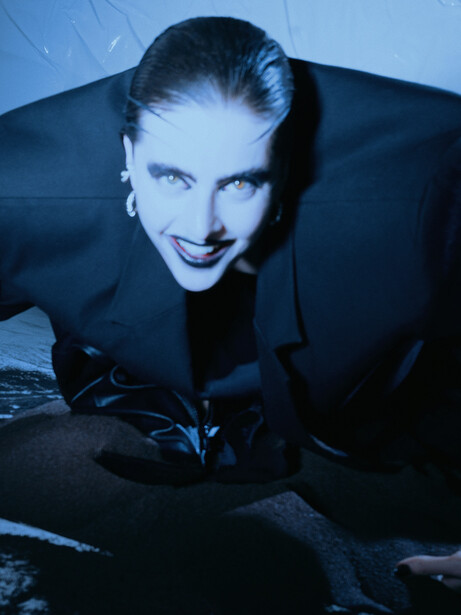 Person in black suit leaning forward against blue-tinted background with dramatic lighting.