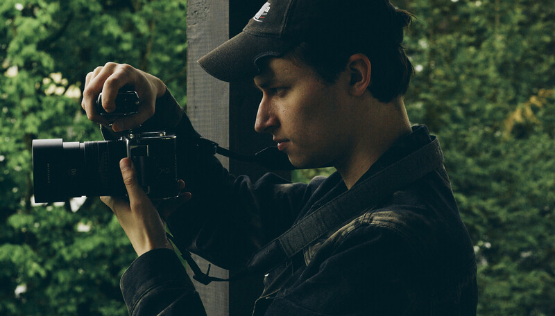 Cinematographer operating a film camera outdoors with ivy-covered background.