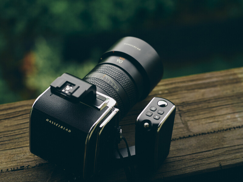 Medium format camera with telephoto lens mounted on wooden surface outdoors.