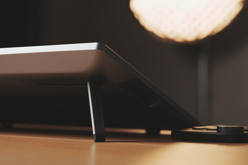 Minimalist desk setup with a monitor and pendant lamp creating warm ambient lighting against a dark background.