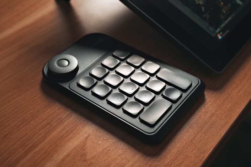 Black mechanical keypad with 20 keys and a rotary dial control on a wooden desk.