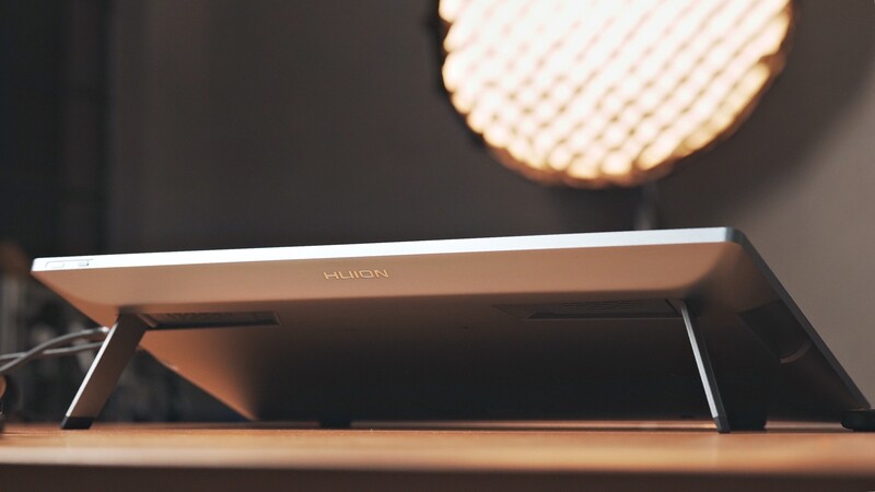 Modern tablet or display device shown at an angle on a wooden surface with studio lighting above.