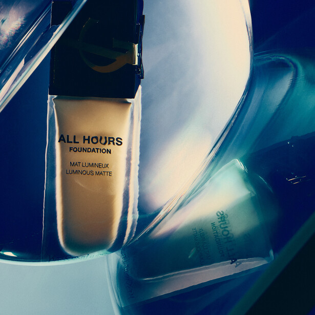 Liquid foundation bottle displayed against blue and white abstract background with fluid swirls.