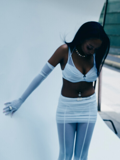 Woman in white crop top and high-waisted skirt posing against white architectural background.