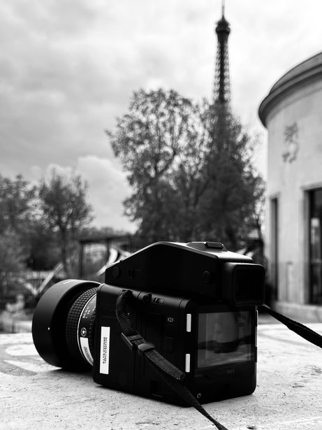 Black camera with lens on stone surface, Eiffel Tower visible in blurred background.