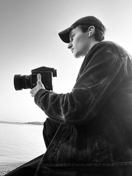 Photographer holding a camera with telephoto lens while positioned in a boat, shooting toward water and sky.