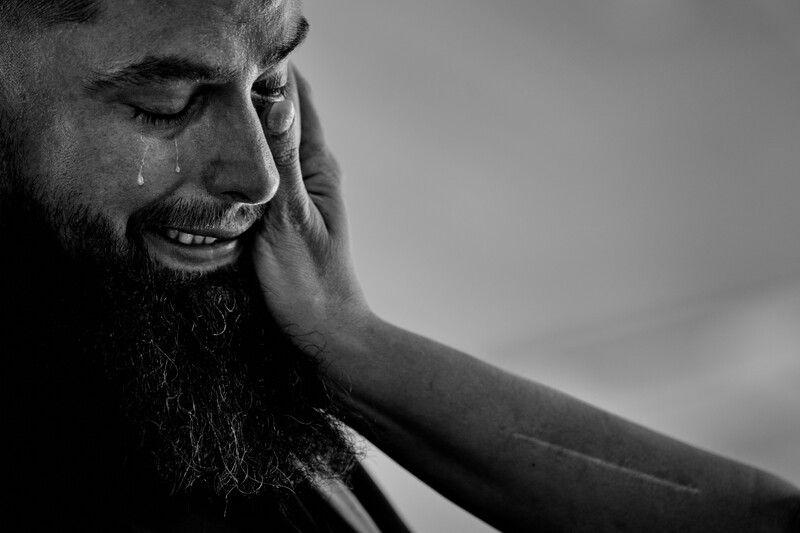 Bearded man with eyes closed, hand to face, with a tear visible in black and white photography.