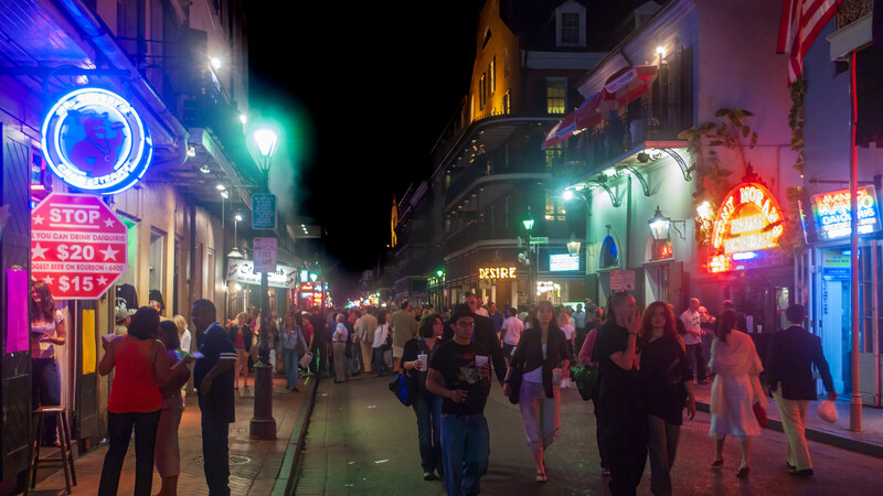 Crowded nighttime street scene with neon signs and pedestrians beneath historic buildings.