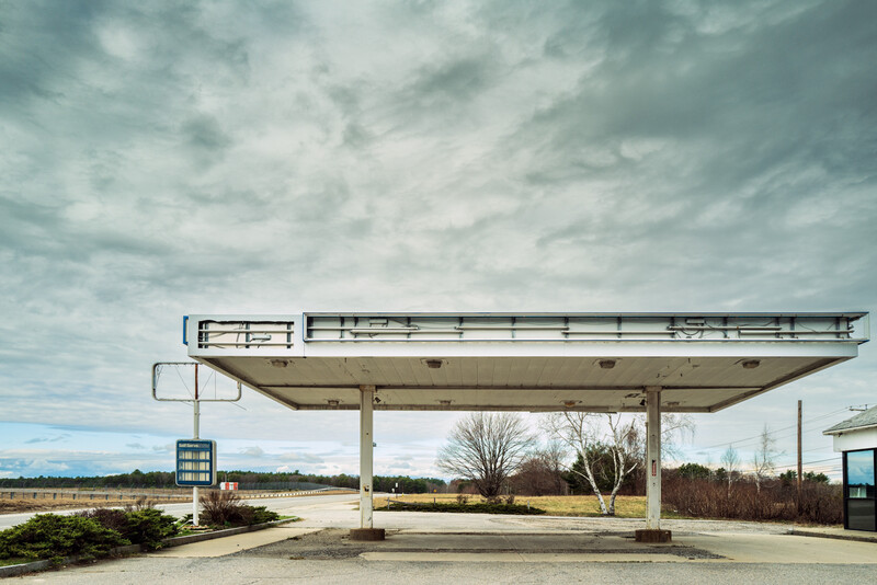 Abandoned gas station with a long canopy structure under a dramatic cloudy sky.