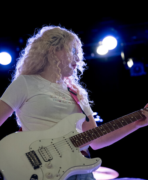 Musician performing with white Stratocaster-style electric guitar under stage lighting.