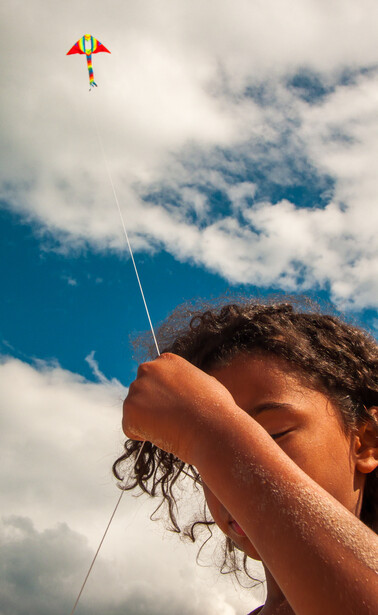 Person's hand holding a kite string against a bright blue sky with white clouds.