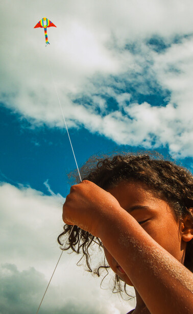 Person's hand holding a kite string against a bright blue sky with white clouds.
