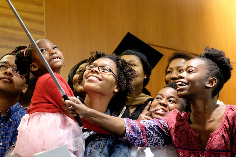 Group of children and adults smiling while looking upward together indoors.