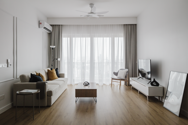 Modern apartment living room with light wood flooring, gray sofa, and floor-to-ceiling curtained doors.