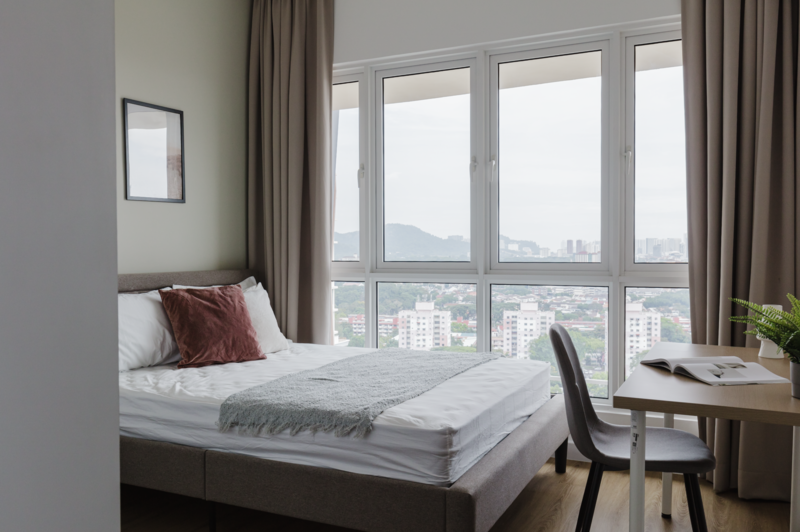 Modern bedroom with floor-to-ceiling windows overlooking a cityscape and mountains in the distance.