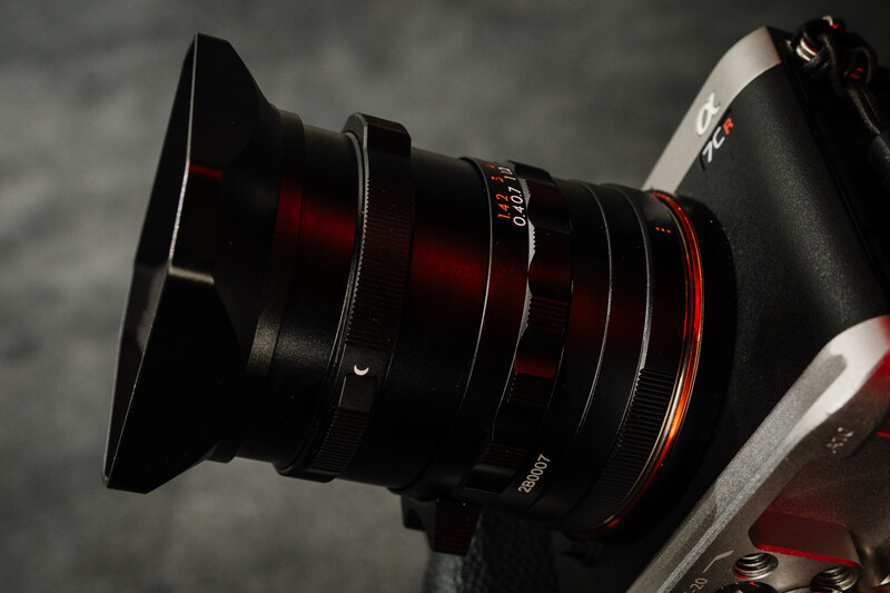Wide-angle lens with red accents mounted on camera body against gray backdrop.