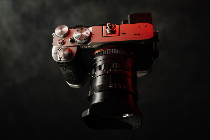 Red mirrorless camera with vintage prime lens mounted on dark background.