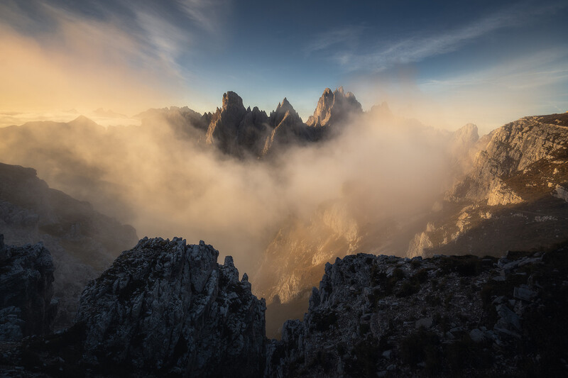 Dramatic mountain peaks rising through dense golden mist at sunrise.