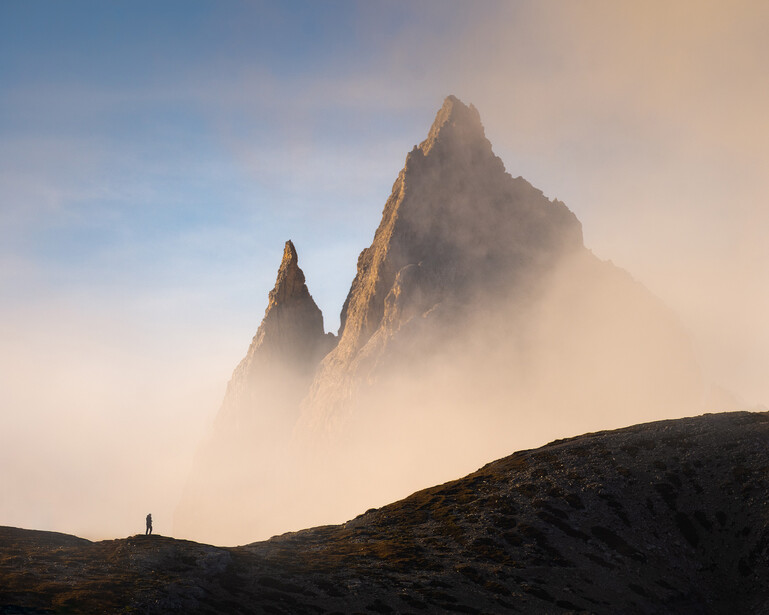 Two jagged mountain peaks rising through dense fog and mist in golden morning light.
