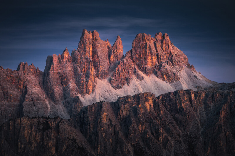 Dramatic mountain peaks with jagged ridges illuminated by golden alpenglow against a deep blue twilight sky.