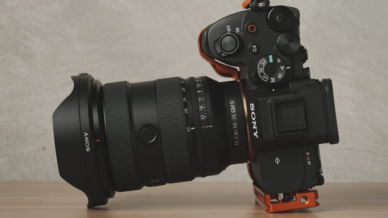 Sony mirrorless camera with wide-angle lens and lens hood mounted on orange grip rig.