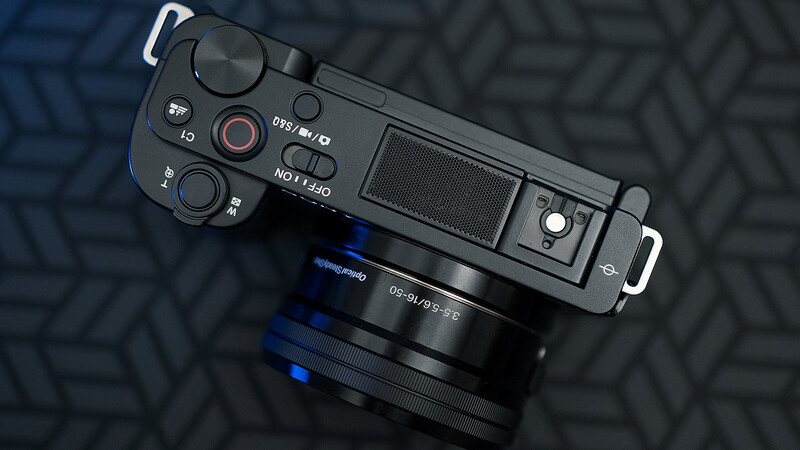 Top-down view of a compact mirrorless camera with attached lens on a textured dark surface.