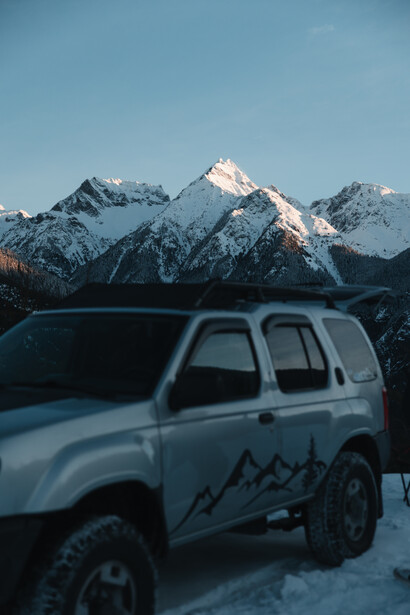 White SUV with mountain graphic decal parked in snow with snow-capped peaks in background.