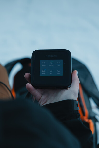 Person holding a compact action camera with small screen against blurred outdoor background.