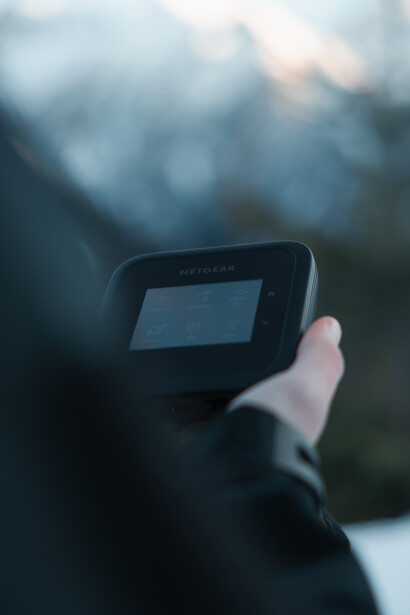 Hand holding a thermal imaging camera against a blurred mountainous landscape background.