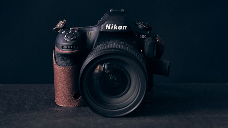 Nikon D850 DSLR camera with attached lens and brown leather grip on dark surface.