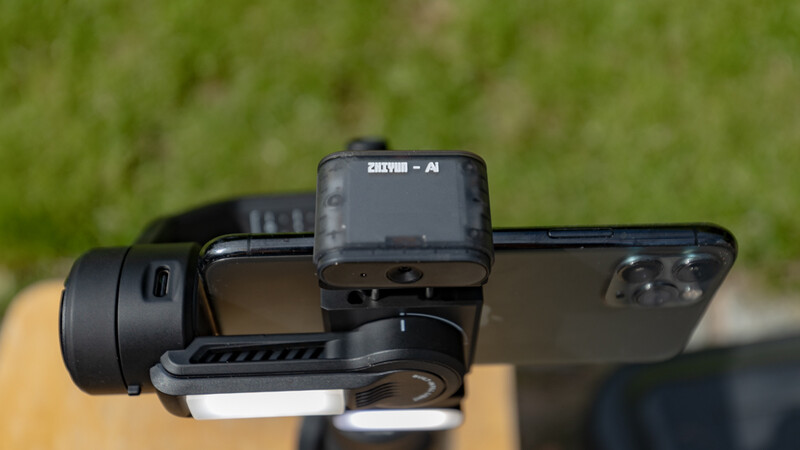 Smartphone mounted on stabilizer rig with auxiliary lens attachment and monitor displayed outdoors.